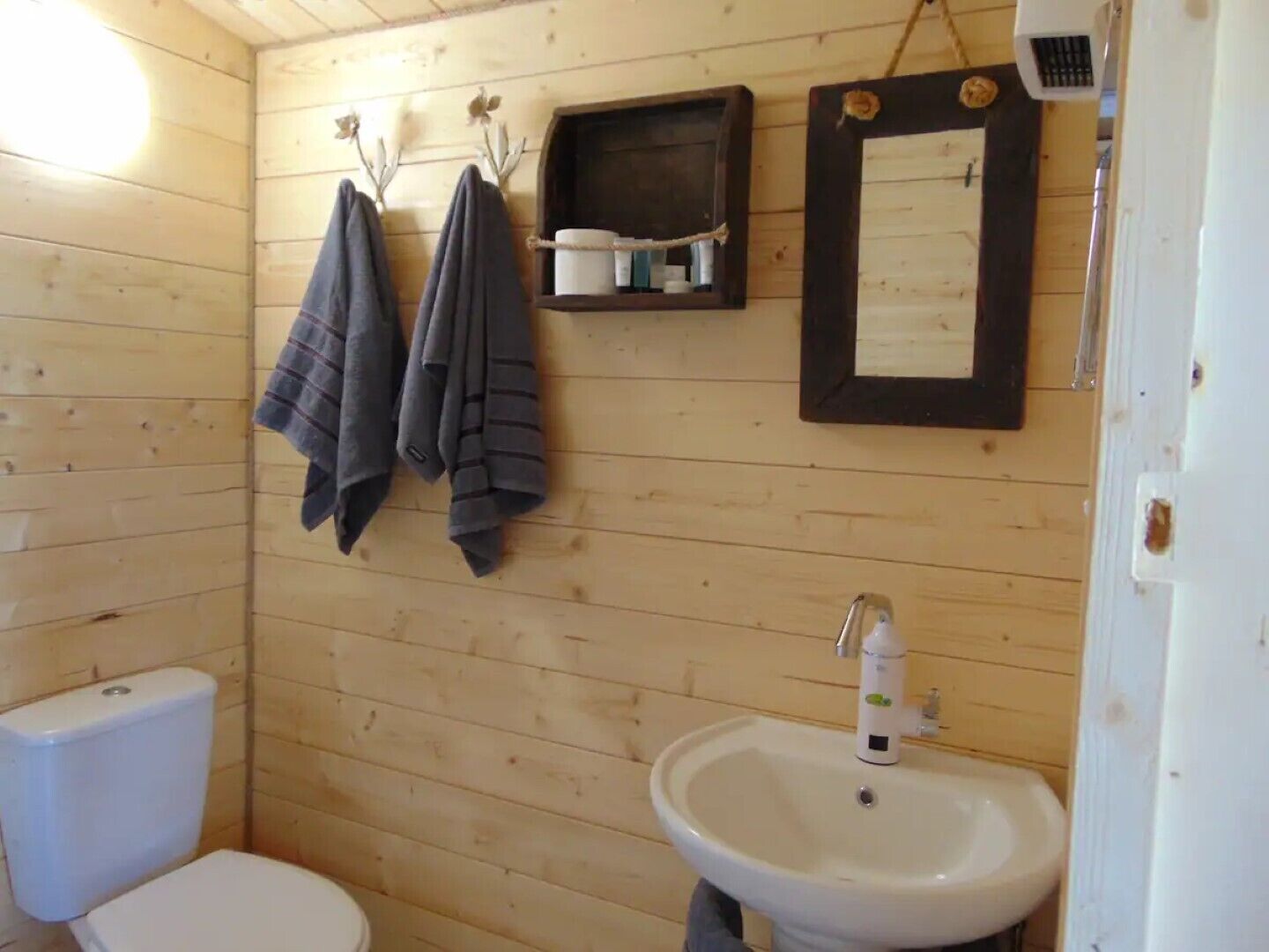 Et lille badeværelse med træpaneler, toilet, håndvask og to håndklæder hængende på kroge.