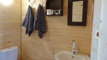 Et lille badeværelse med træpaneler, toilet, håndvask og to håndklæder hængende på kroge.