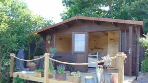 A rustic wooden cabin with a porch, potted plants, and a rope barrier. - Private Quiet Cabin, overlooking Paddocks Vineyards and Pine Forest (East Sussex)