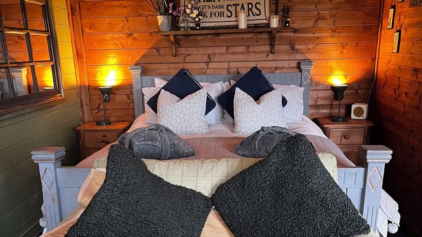 A cozy bedroom with a wooden headboard, a bed with patterned pillows, bedside lamps, and a decorative sign on the wall. - Private Quiet Cabin, overlooking Paddocks Vineyards and Pine Forest (East Sussex)