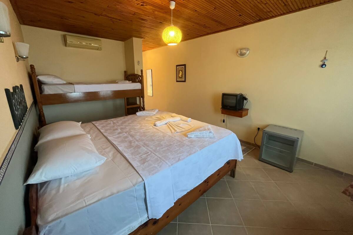 Ein Zimmer mit Holzboden, einem Bett mit weißer Bettdecke, einem Fernseher auf einem Regal und einem kleinen Schrank.