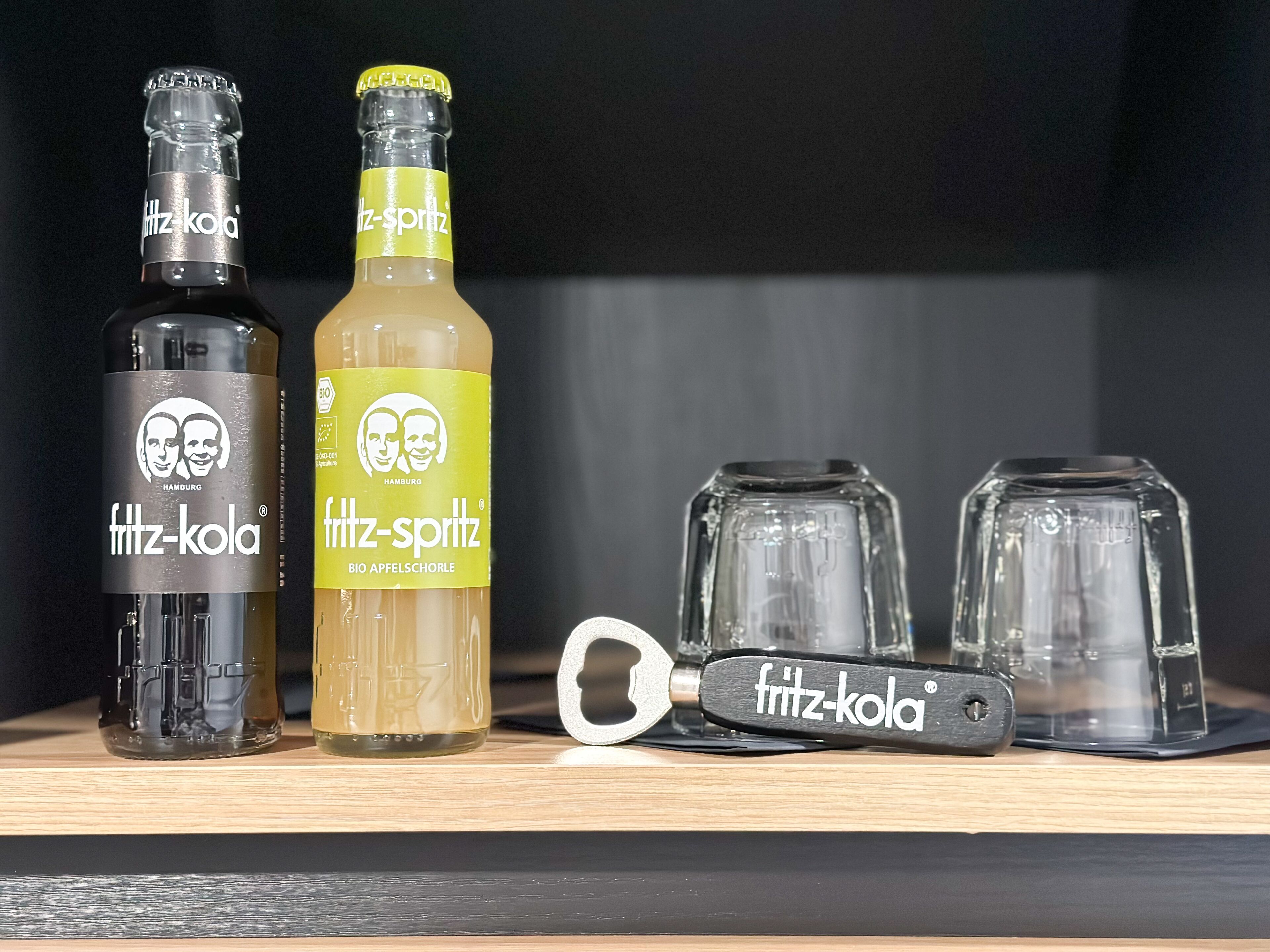 Two bottles of Fritz-Kola, a bottle of Fritz-Spritz, and two glasses on a wooden surface.