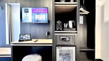Ein modernes Hotelzimmer mit Flachbildfernseher, der eine Willkommensnachricht anzeigt, einer Minibar, einer Kaffeemaschine und einem kleinen Kühlschrank.