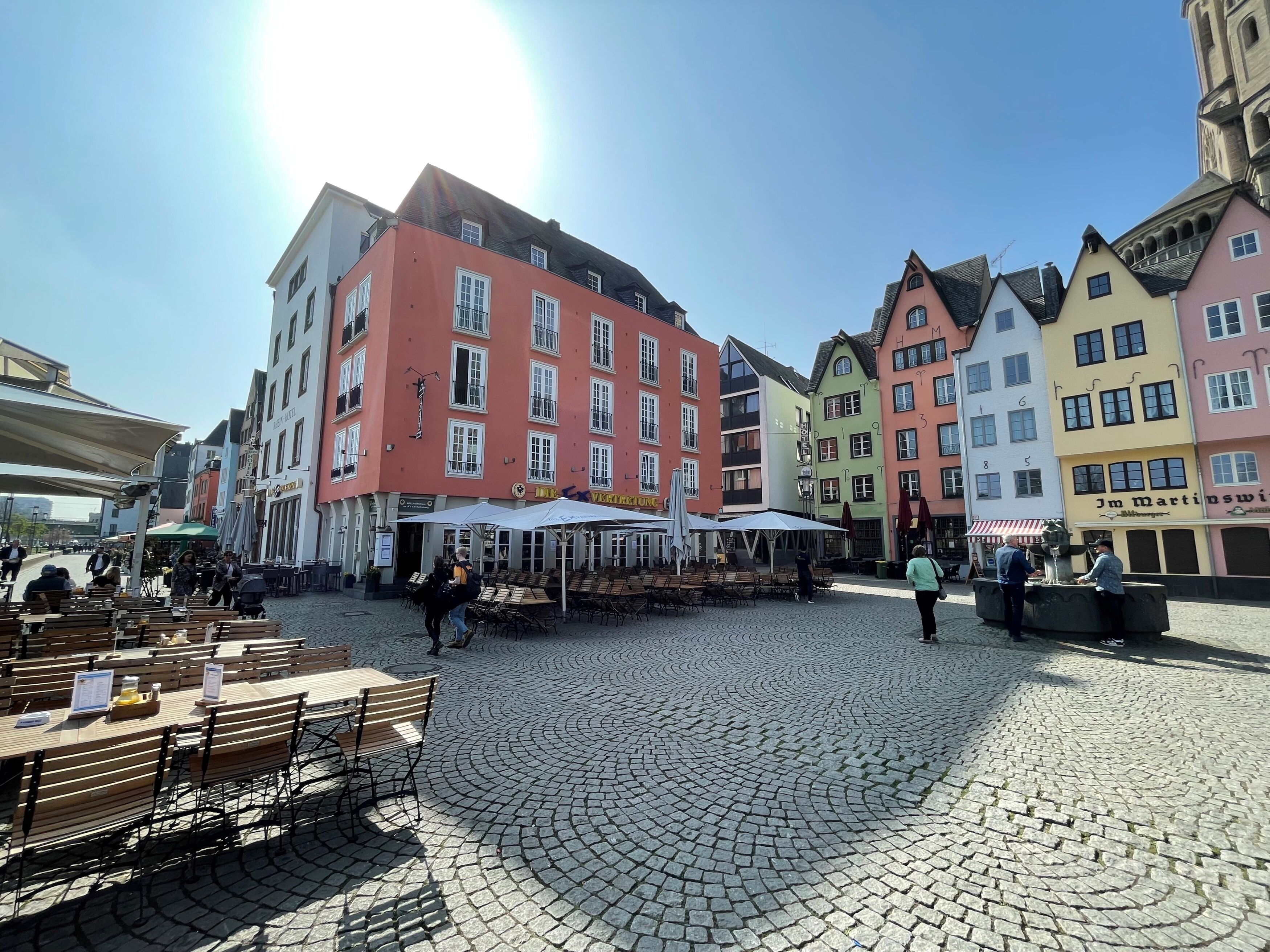 Ein Kopfsteinpflasterplatz mit Außenbestuhlung und bunten Gebäuden.