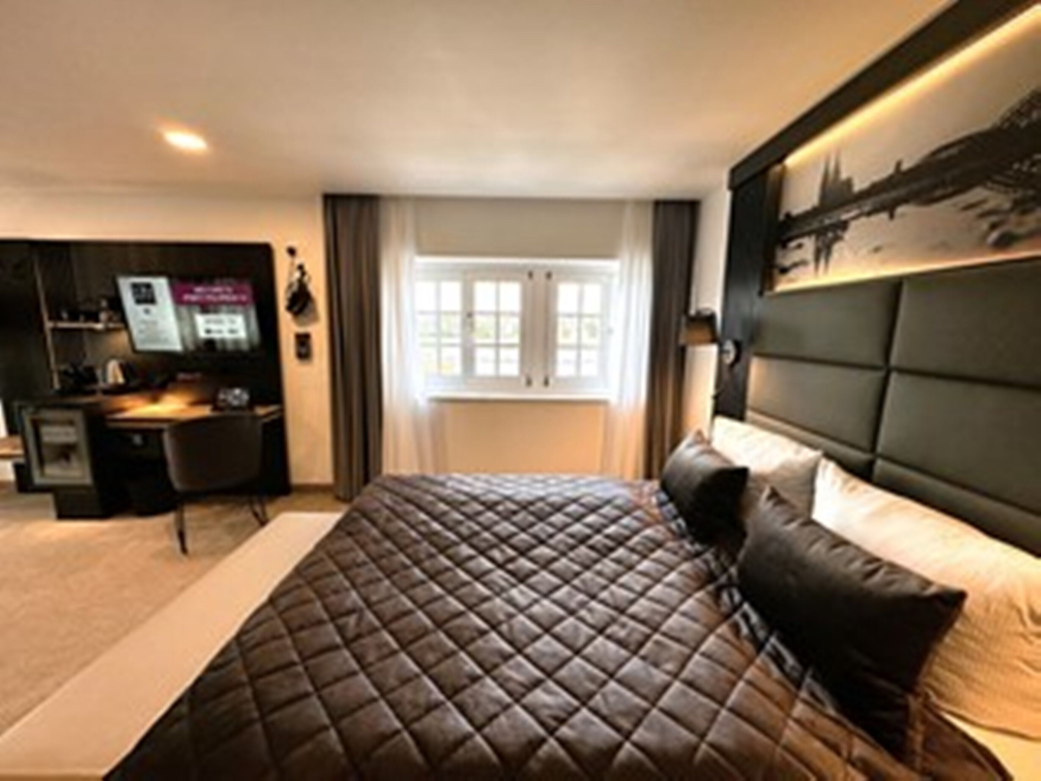 A modern hotel room with a large bed, a desk, and a cityscape view.