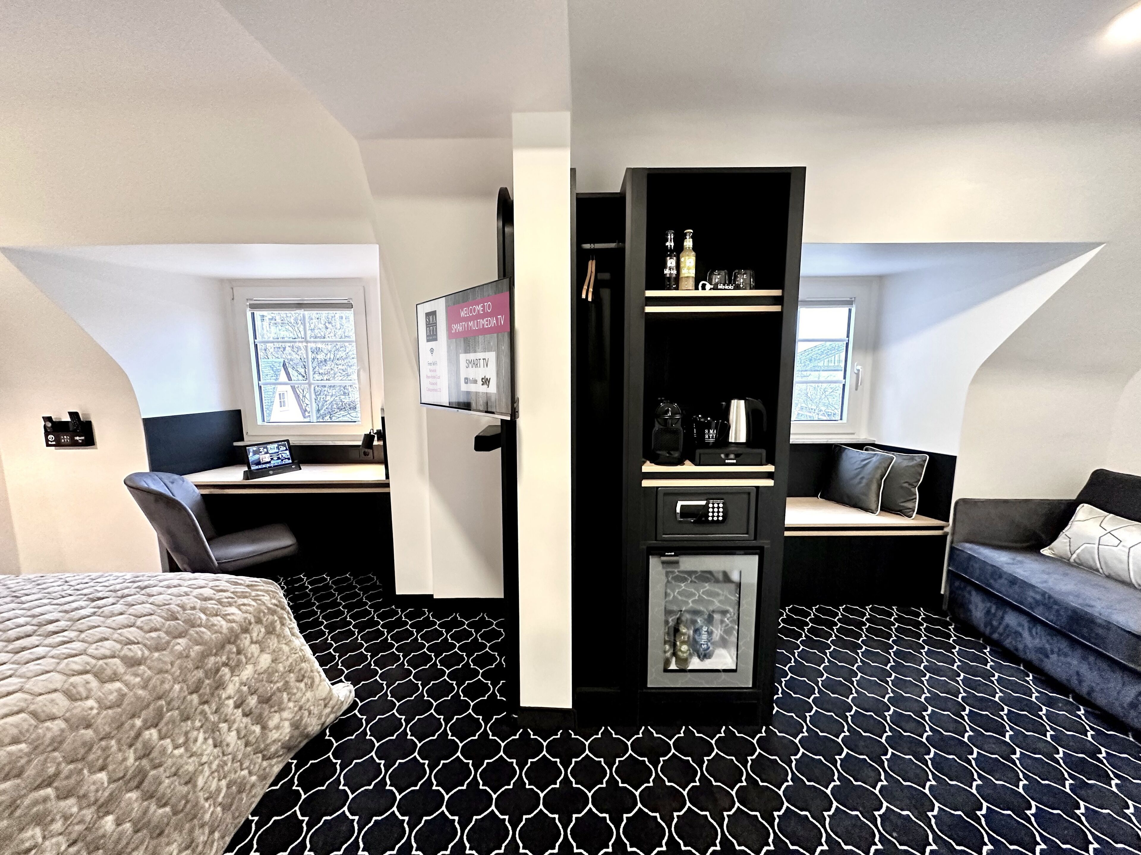Una habitación de hotel moderna con una cama, un escritorio con una computadora, un televisor y una zona de estar con un sofá.