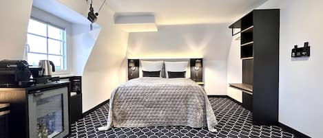 Un dormitorio moderno con piso de diseño geométrico, cama con cabecera acolchada, escritorio con cafetera y televisor montado en la pared.