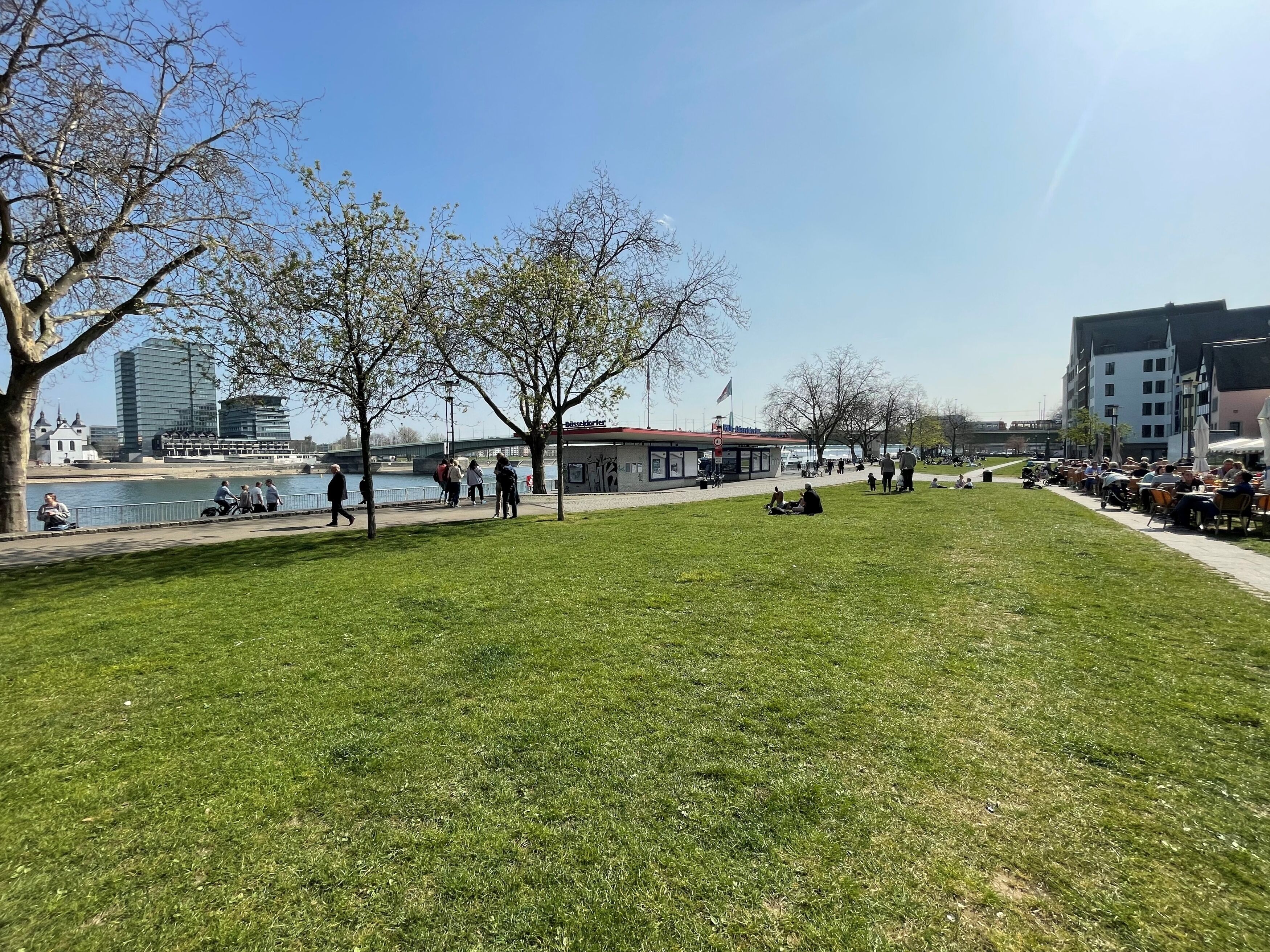 A park with a river, benches, and a building with a red roof.
