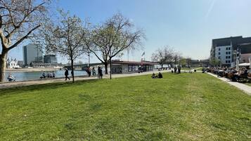 A park with a river, benches, and a building with a red roof.