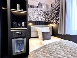 Una habitación de hotel moderna con cama, minibar, máquina de café y una pared con numerosas llaves.
