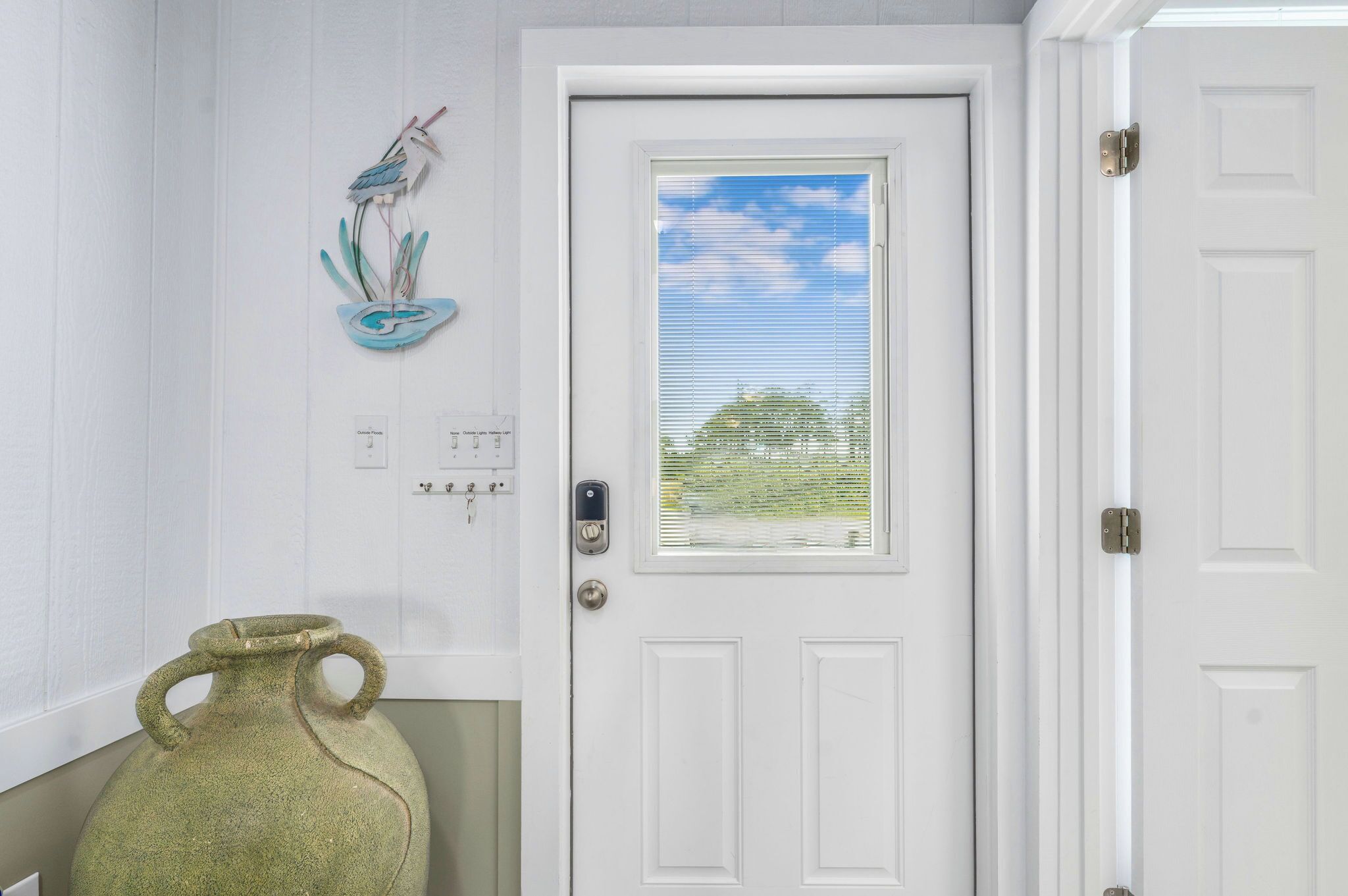A white door with a window, a wall-mounted bird sculpture, and a green vase.