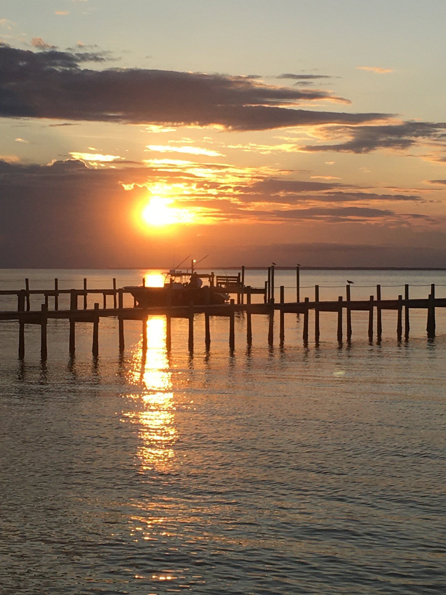 A sunset over a calm body of water with a dock extending into the water.