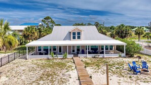Una casa frente a la playa con un porche cubierto, una terraza de madera y un jardín de arena.