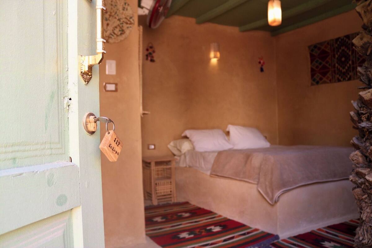 A room with a bed, a door with a key, and a patterned rug.