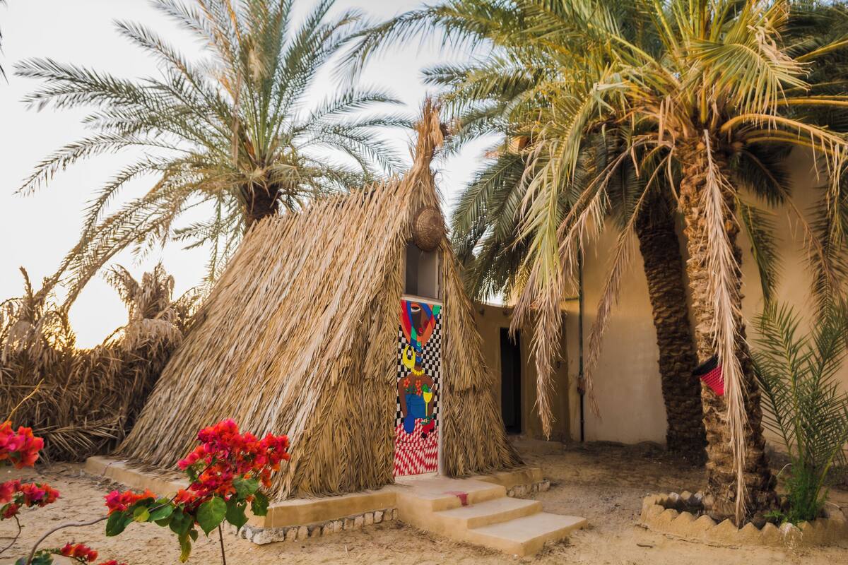 A traditional hut with thatched walls and a palm tree in the foreground.