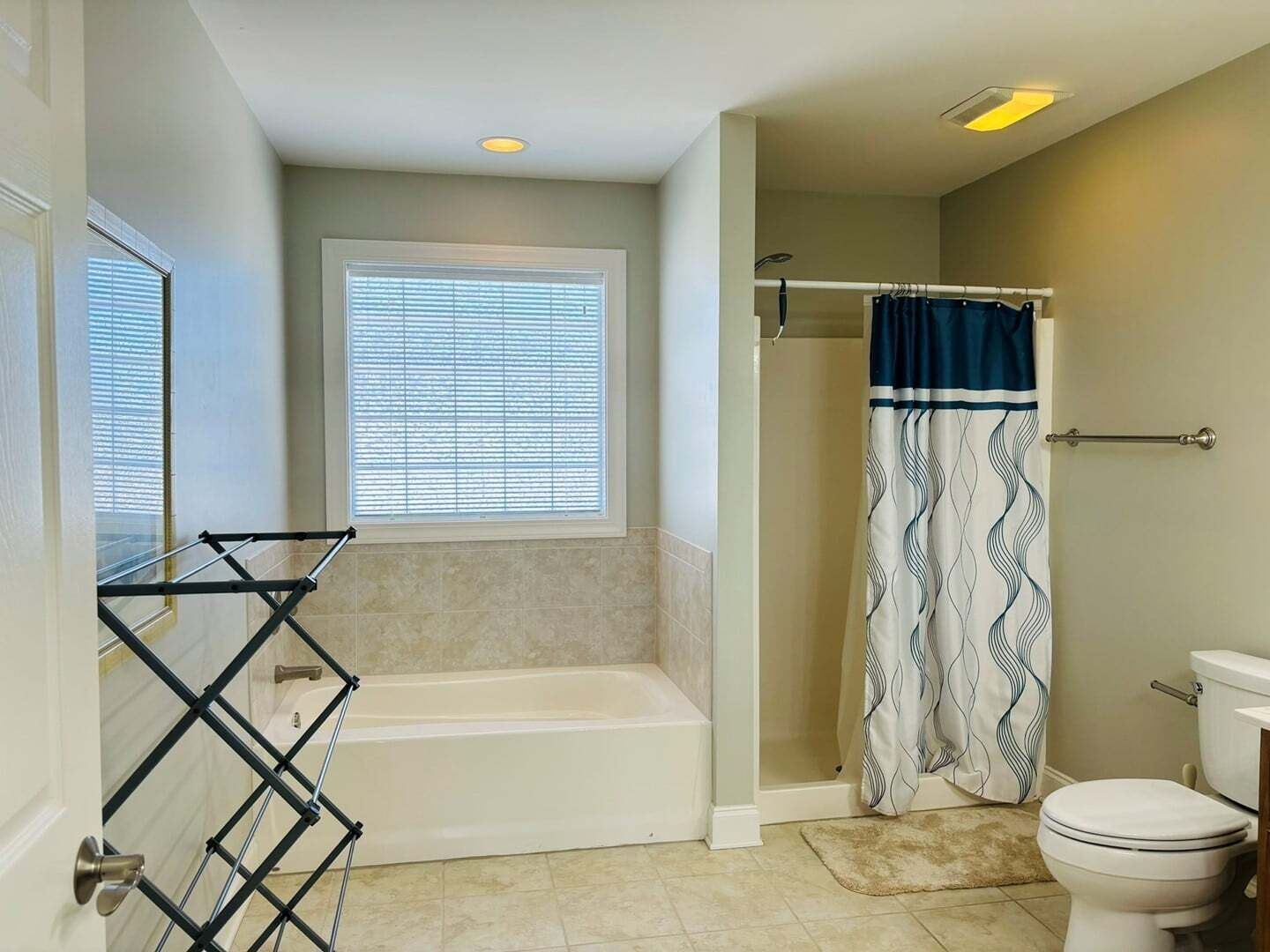 A bathroom with a bathtub, shower curtain, toilet, and a window with blinds.