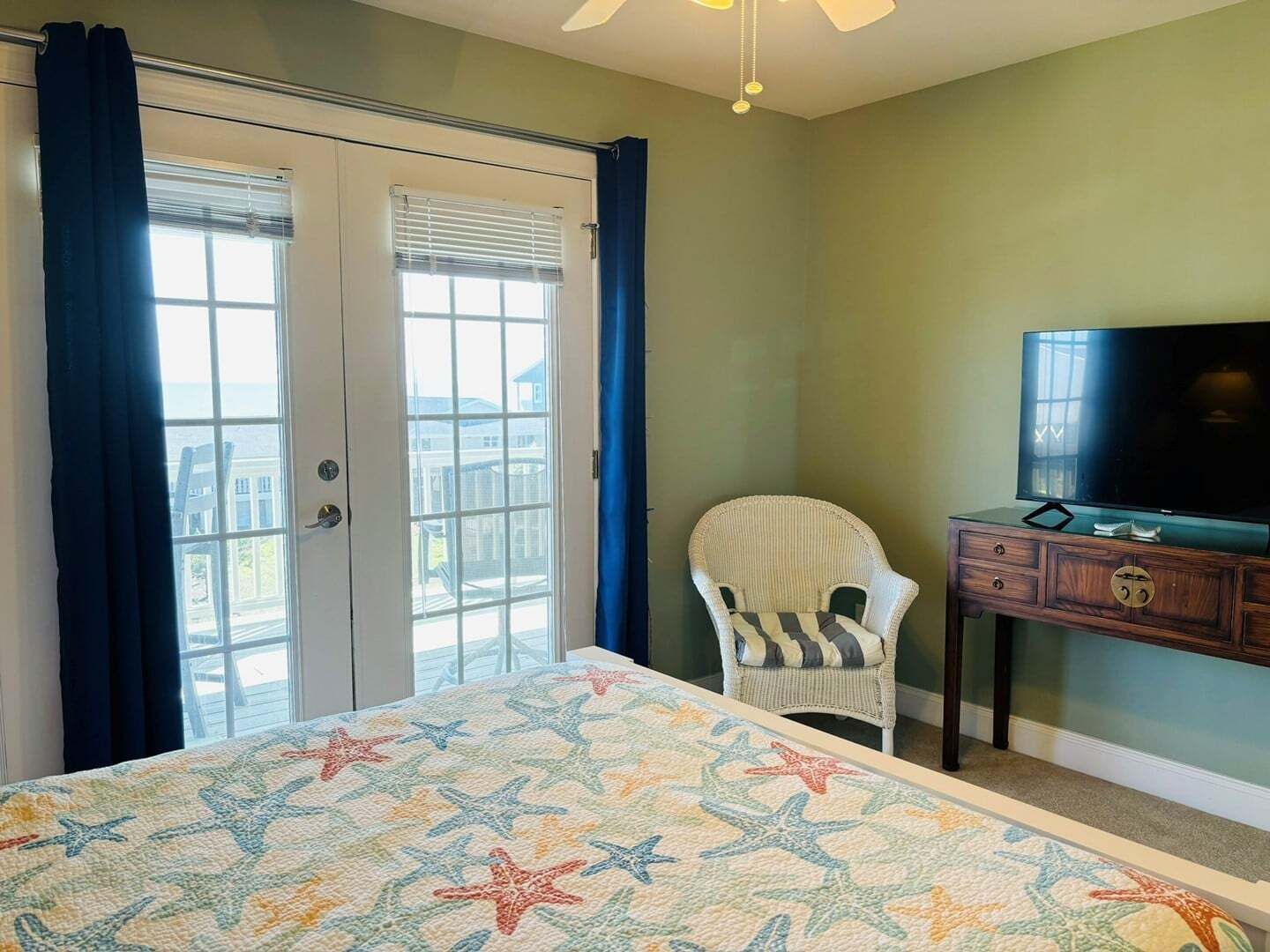 A bedroom with a bed, a chair, a TV, and a balcony with curtains.