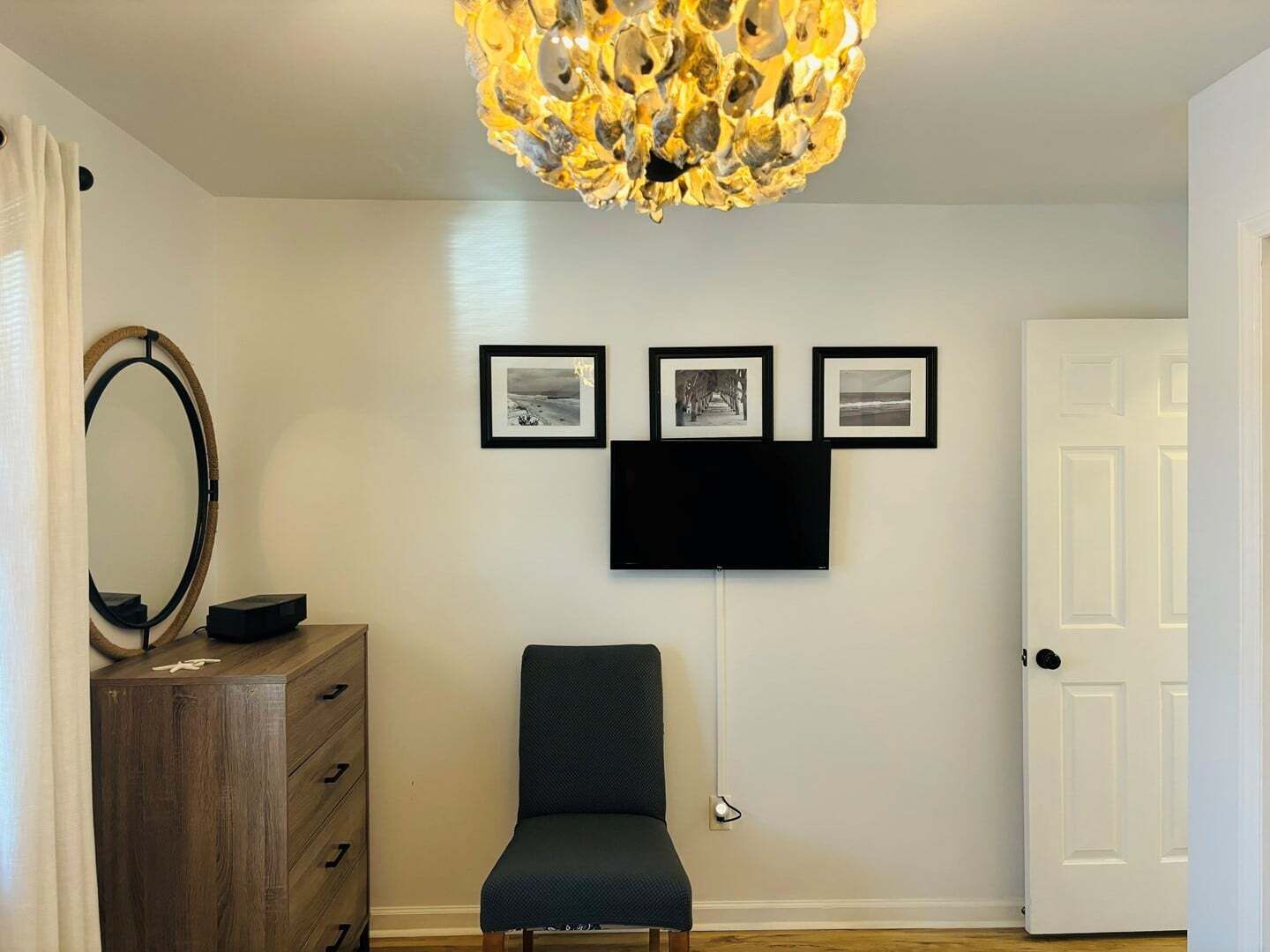 A room with a wooden dresser, a chair, a wall-mounted TV, and three framed pictures.
