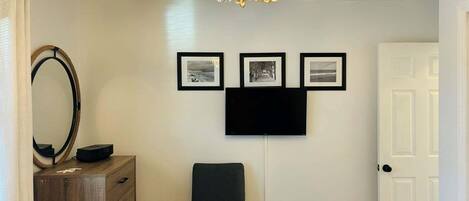 A room with a wooden dresser, a chair, a wall-mounted TV, and three framed pictures.