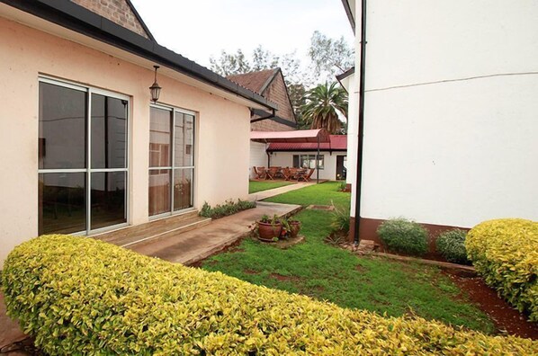 A house with a large sliding glass door, a small patio with a table and chairs, and well-maintained green lawns.