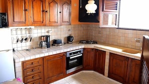 A kitchen with wooden cabinets, a stove, a sink, and a hanging light fixture. - Residence Le Citron Vert (Rivière-Salée)