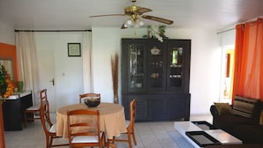 A dining area with a round table and chairs, a ceiling fan, and a cabinet with glass doors. - Residence Le Citron Vert (Rivière-Salée)