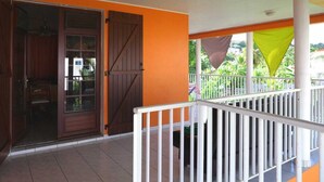A covered outdoor area with a wooden door, white railing, and orange walls. - Residence Le Citron Vert (Rivière-Salée)