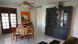 A living room with a dining area, a cabinet with glass doors, and a ceiling fan. - Residence Le Citron Vert (Rivière-Salée)