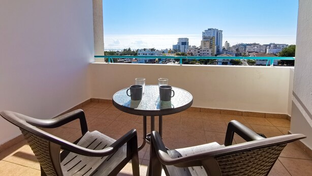 A balcony with a table and chairs, a view of a cityscape, and a clear sky. - Off Course Seaview Apartment (Larnaca)