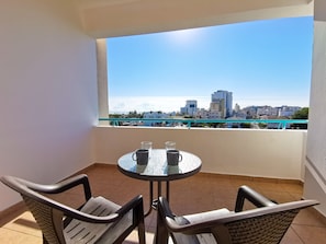A balcony with a table and chairs, a view of a cityscape, and a clear sky.