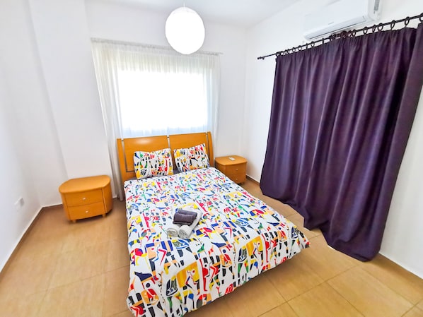 Un dormitorio con cama, mesita de noche, cómoda, ventana con cortinas e iluminación en el techo.