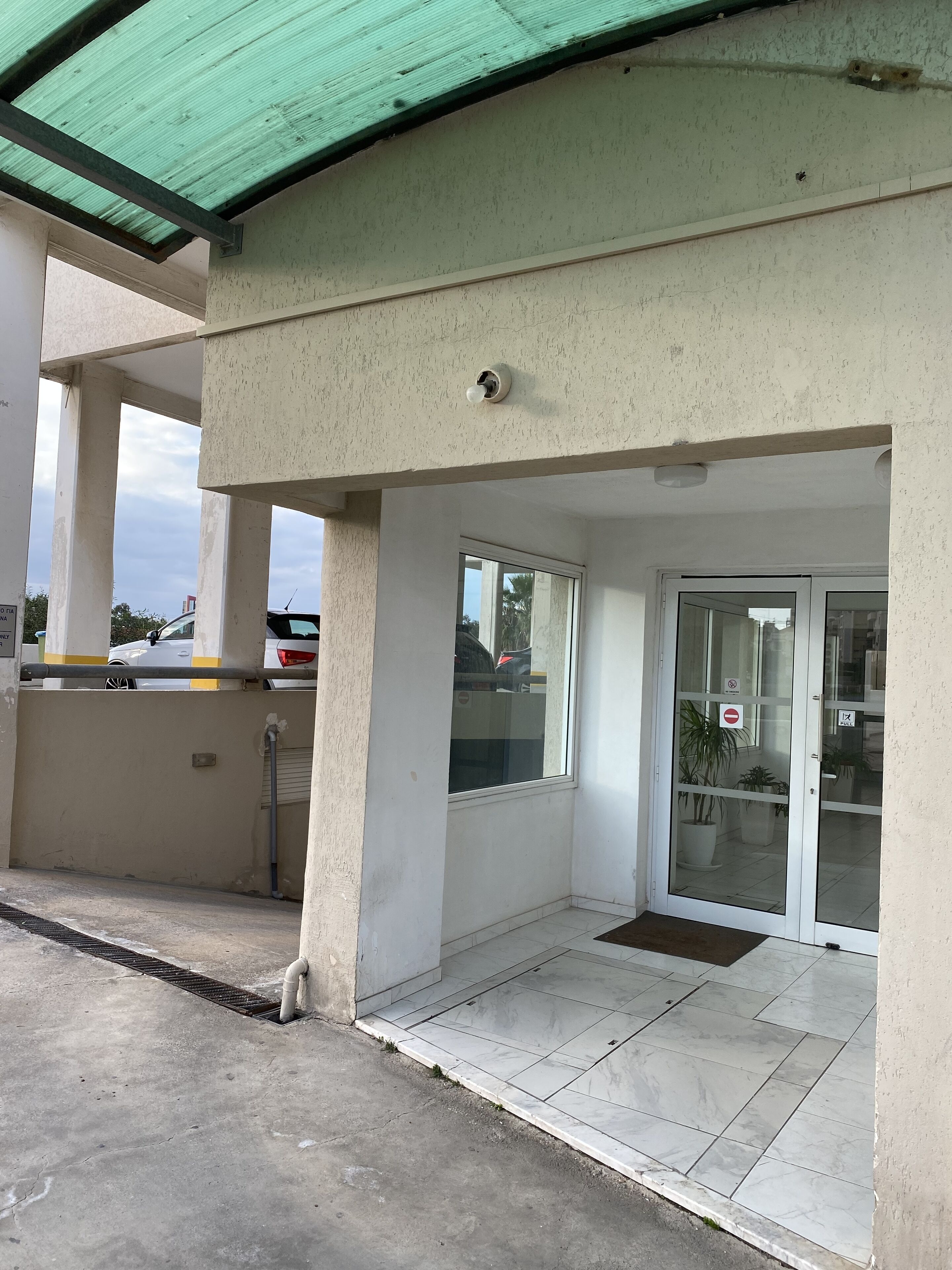 A building entrance with a green roof, a glass door with a 'No Entry' sign, and a tiled floor.
