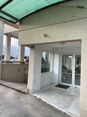 Una entrada de edificio con techo verde, puerta de vidrio con letrero de 'Prohibido el paso' y piso de baldosas.