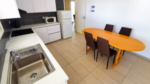 A modern kitchen with white cabinets, a built-in microwave, a refrigerator, and a dining area with an orange table and four chairs. - Off Course Seaview Apartment (Larnaca)