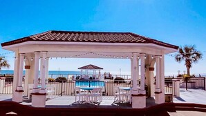 A covered outdoor area with a pool, white chairs, and tables, and a view of the ocean. - 411-B Villa Capriani: Ocean Views & Beach Bliss! (North Topsail Beach)