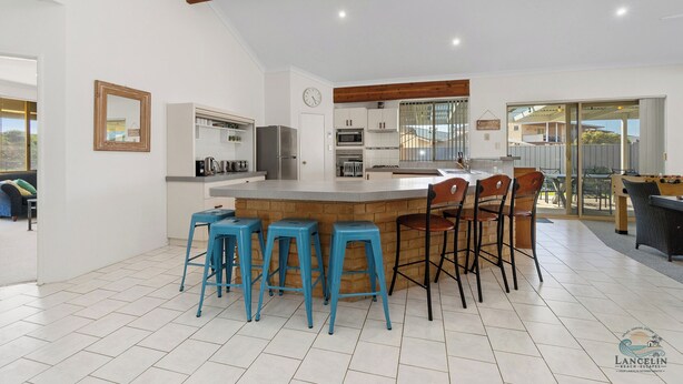 Une cuisine moderne dotée d’un îlot central, de tabourets de bar et d’un coin repas avec des chaises.
