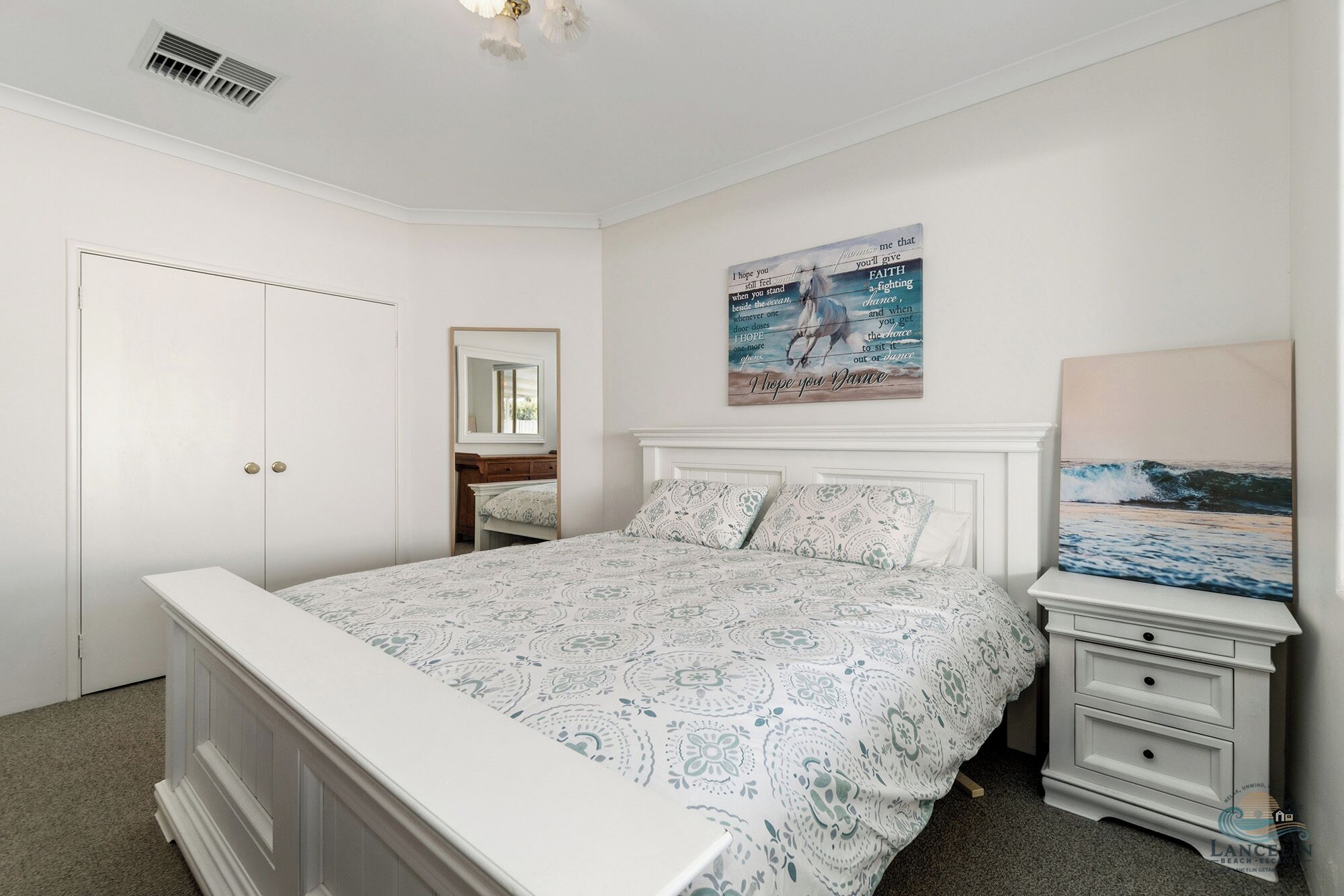 A bedroom with a bed, a nightstand, a dresser, a mirror, and a wall with a painting.