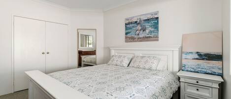 A bedroom with a bed, a nightstand, a dresser, a mirror, and a wall with a painting.