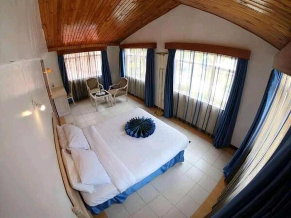 A bedroom with a large bed, two chairs, and a wooden ceiling.