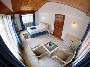 A hotel room with a bed, a desk, two chairs, a small table, a wardrobe, and a window with curtains. - Stay.Plus Hurlingham B&B Suite (Nairobi)
