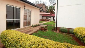 A house with a large sliding glass door, a well-maintained lawn, and a small patio area. - Stay.Plus Hurlingham B&B Suite (Nairobi)