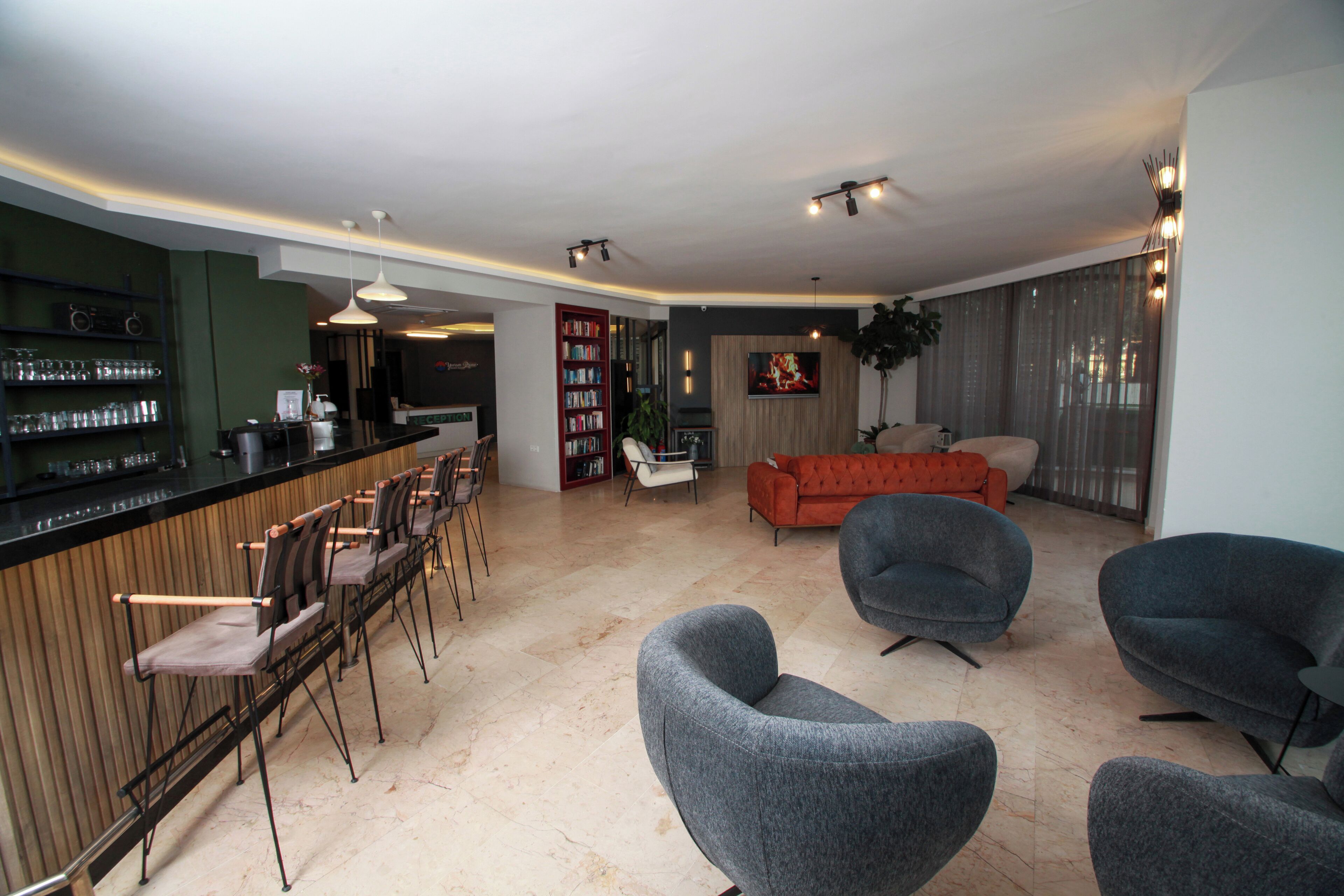 A modern living room with a bar area, grey armchairs, a red sofa, and a bookshelf.