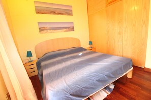 A bedroom with a bed, wooden wardrobe, two bedside tables with lamps, and two wall-mounted pictures.