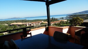 A balcony with a table and chairs, overlooking a coastal landscape with buildings and a body of water. - Tanca Manna three bedrooms apartment 3 bedrooms 2 bathrooms large sea view (Cannigione)