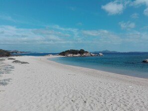 A beach with white sand, clear blue water, and a rocky outcrop with vegetation. - Tanca Manna three bedrooms apartment 3 bedrooms 2 bathrooms large sea view (Cannigione)