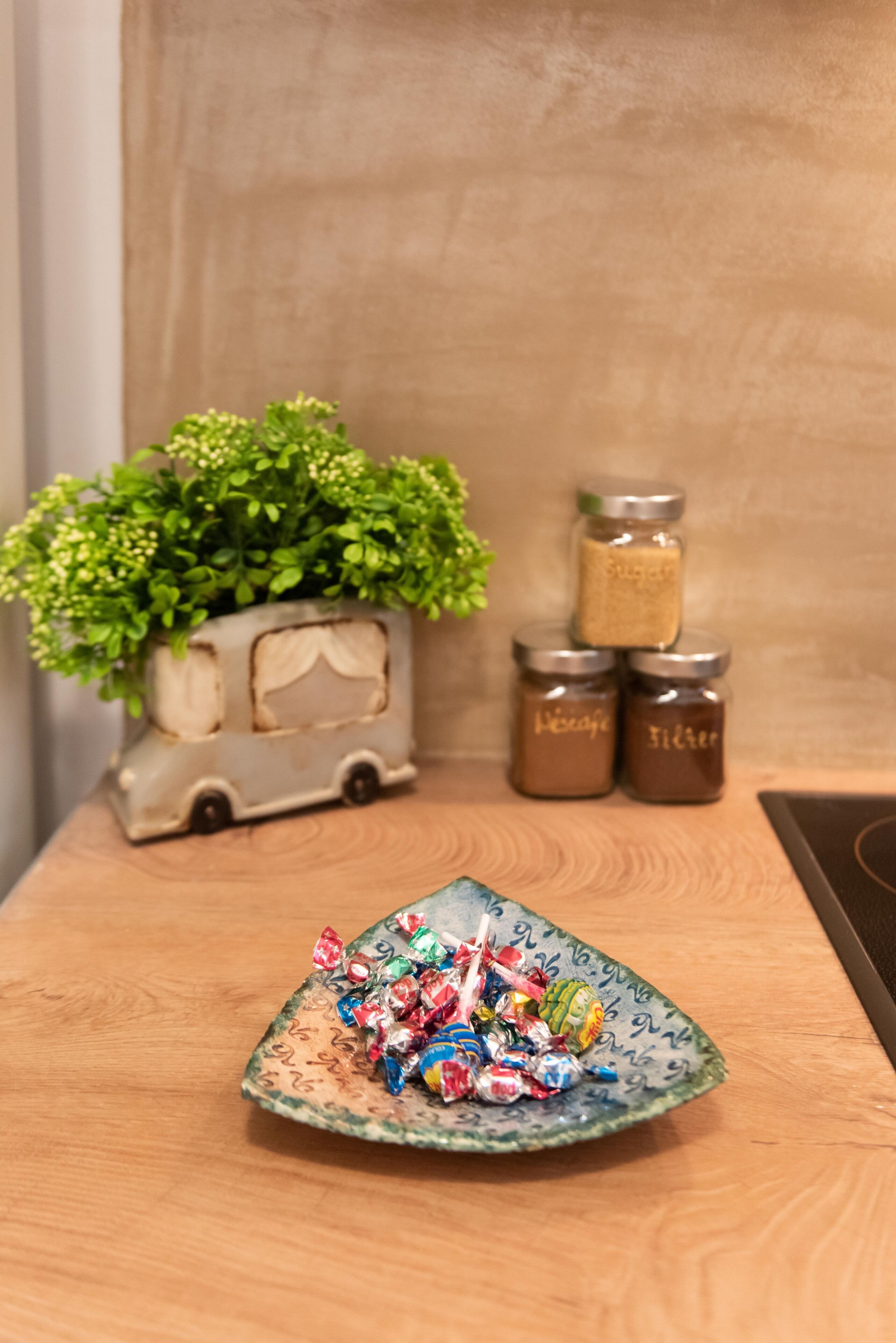 A wooden table with a decorative plate of colorful candies, a small potted plant, and three spice jars.