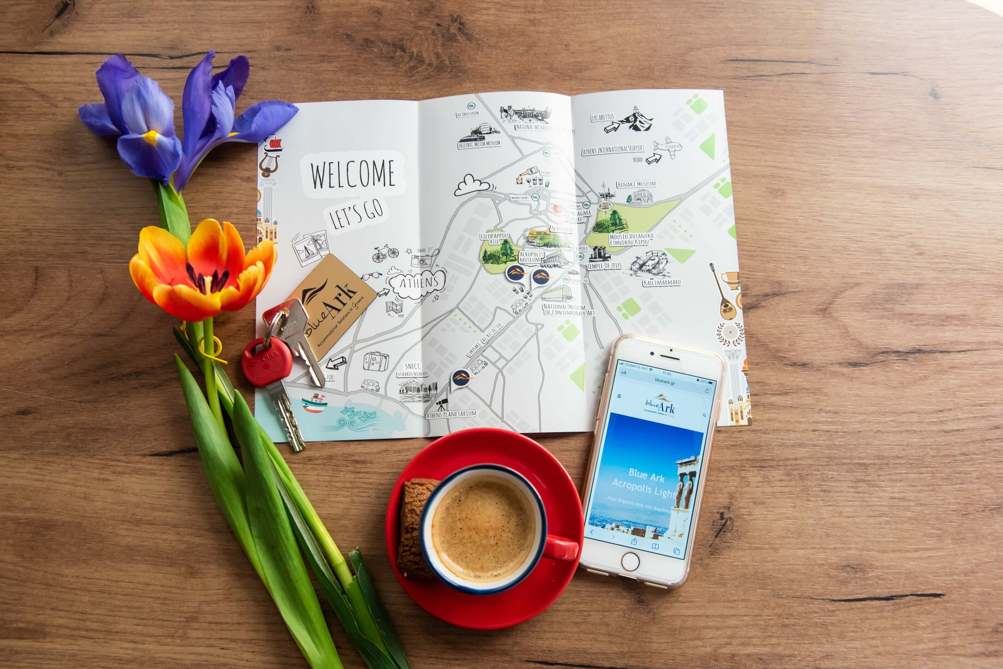 En resekarta, en smartphone, en kopp kaffe och blommor på ett träbord.