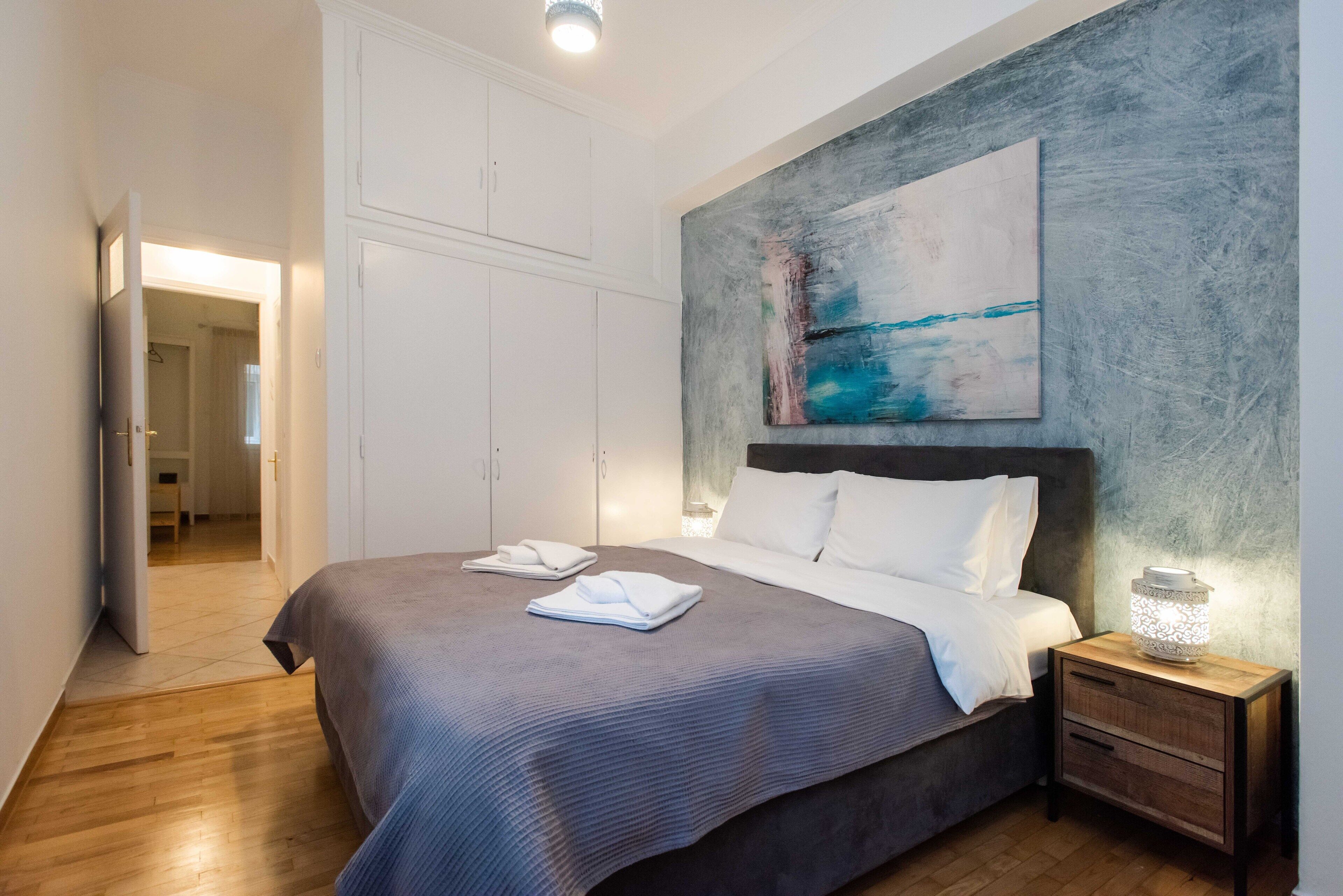 A bedroom with a large bed, a nightstand with a lamp, and a painting on the wall.