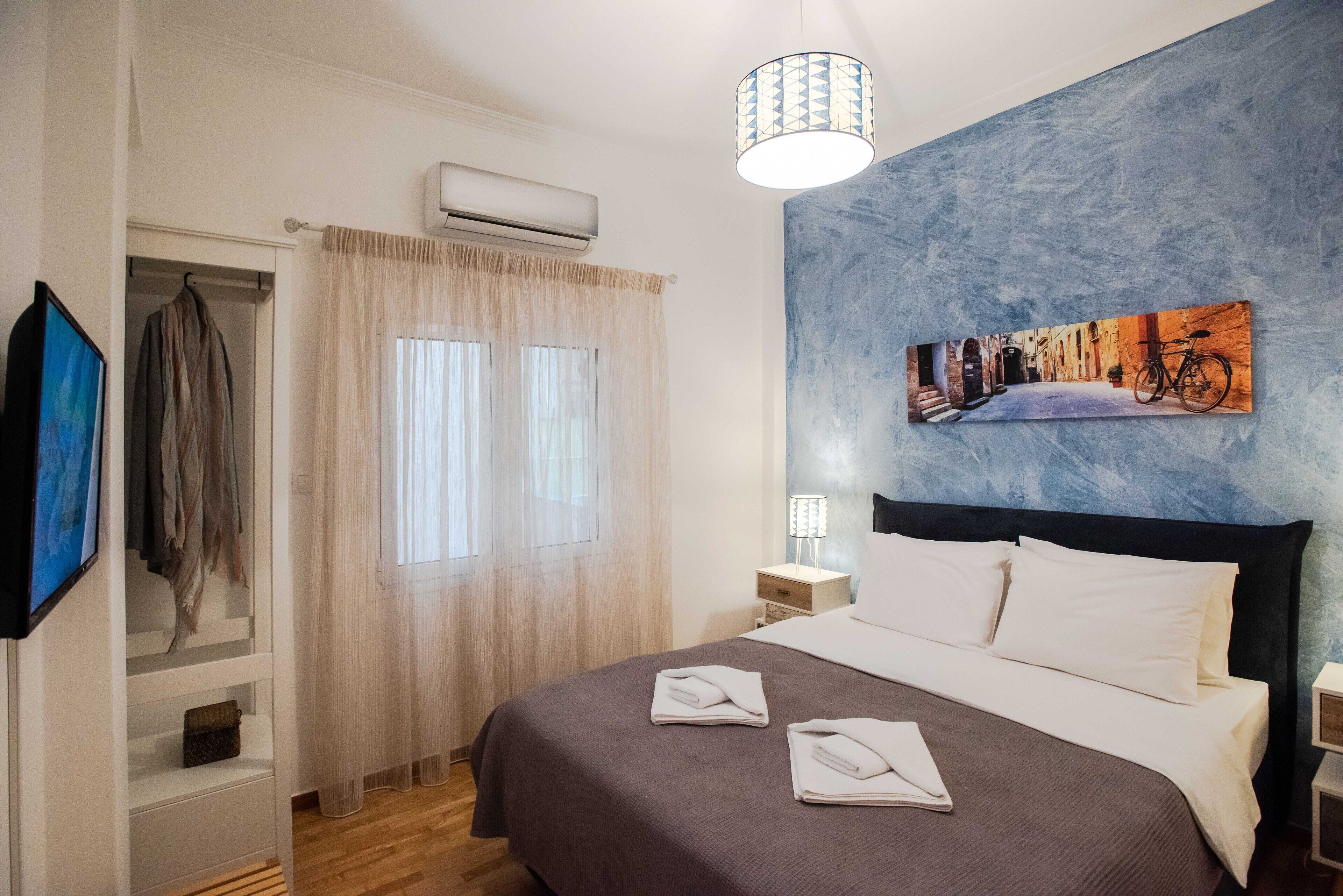 Une chambre d’hôtel avec un lit, un tableau au mur, un appareil de climatisation et un téléviseur fixé au mur.