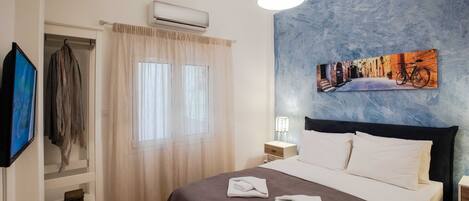 Une chambre d’hôtel avec un lit, un tableau au mur, un appareil de climatisation et un téléviseur fixé au mur.